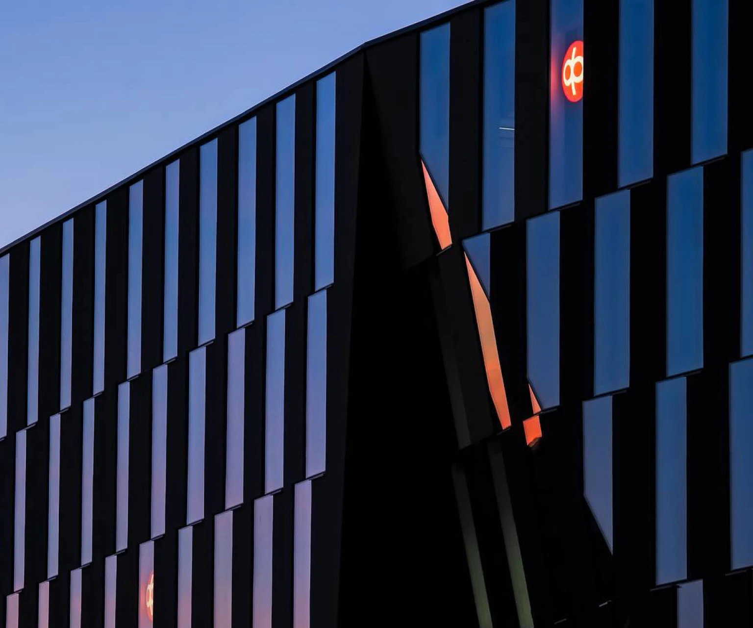 Modern office building with glass facade reflecting the sky and OP Financial Group logo illuminated.