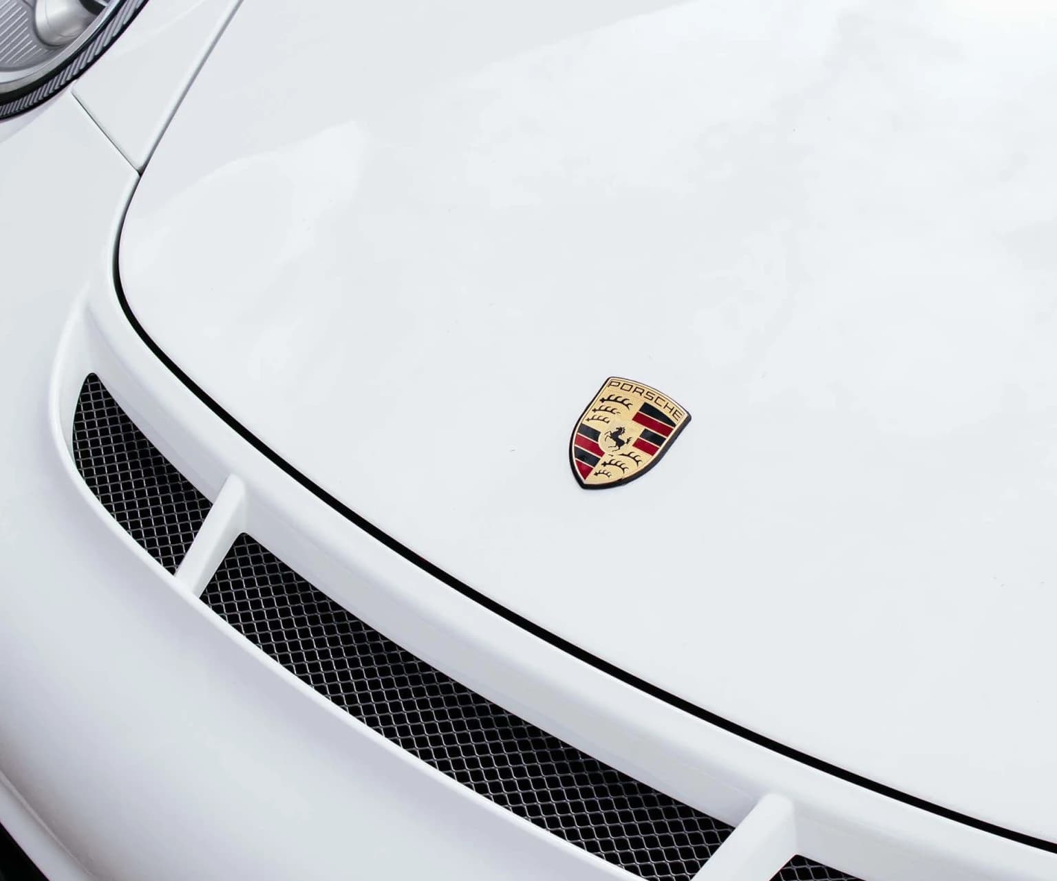 Close-up of Porsche logo on the hood of a white sports car.