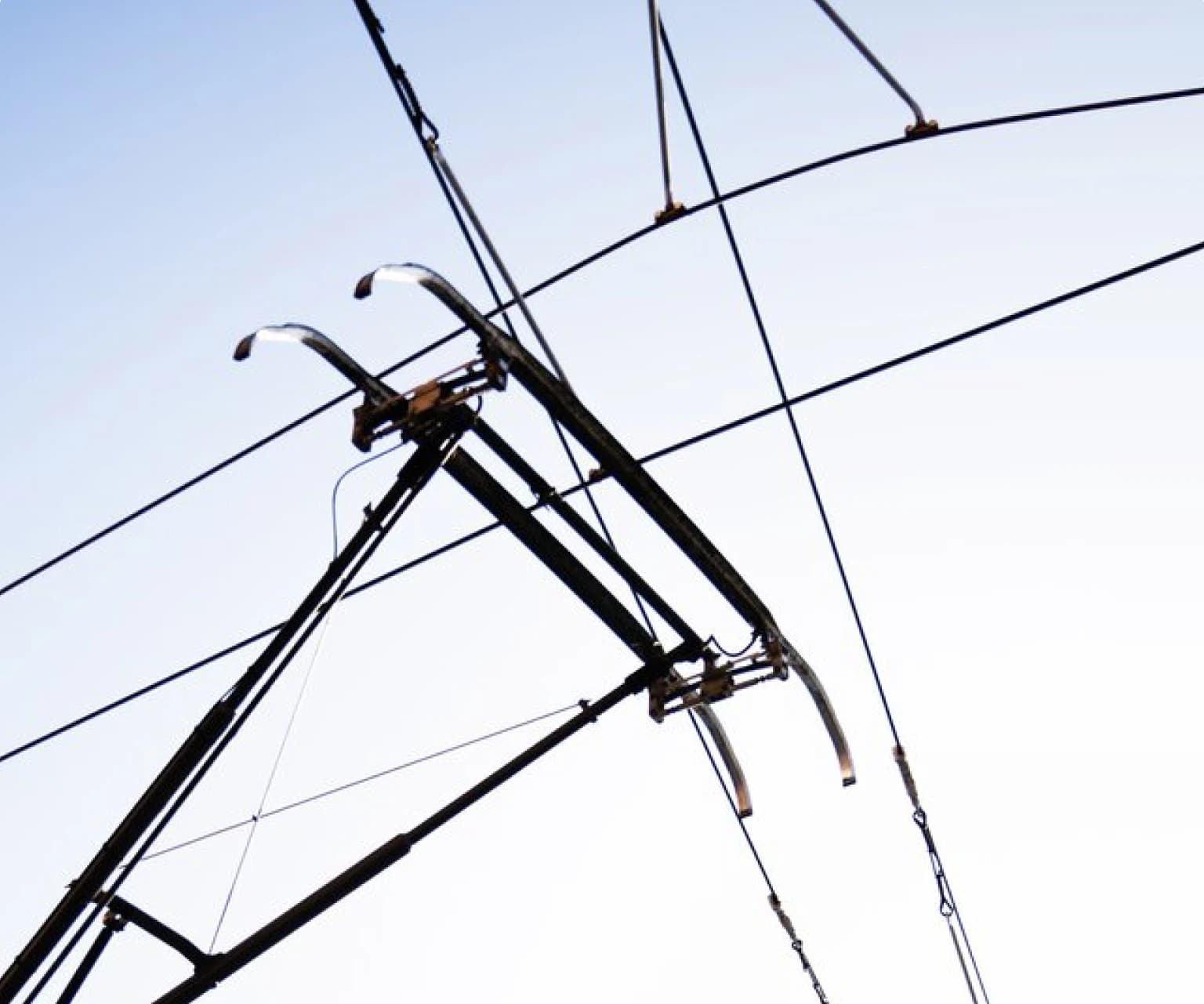 Close-up of overhead electric power lines and pantograph against the sky.