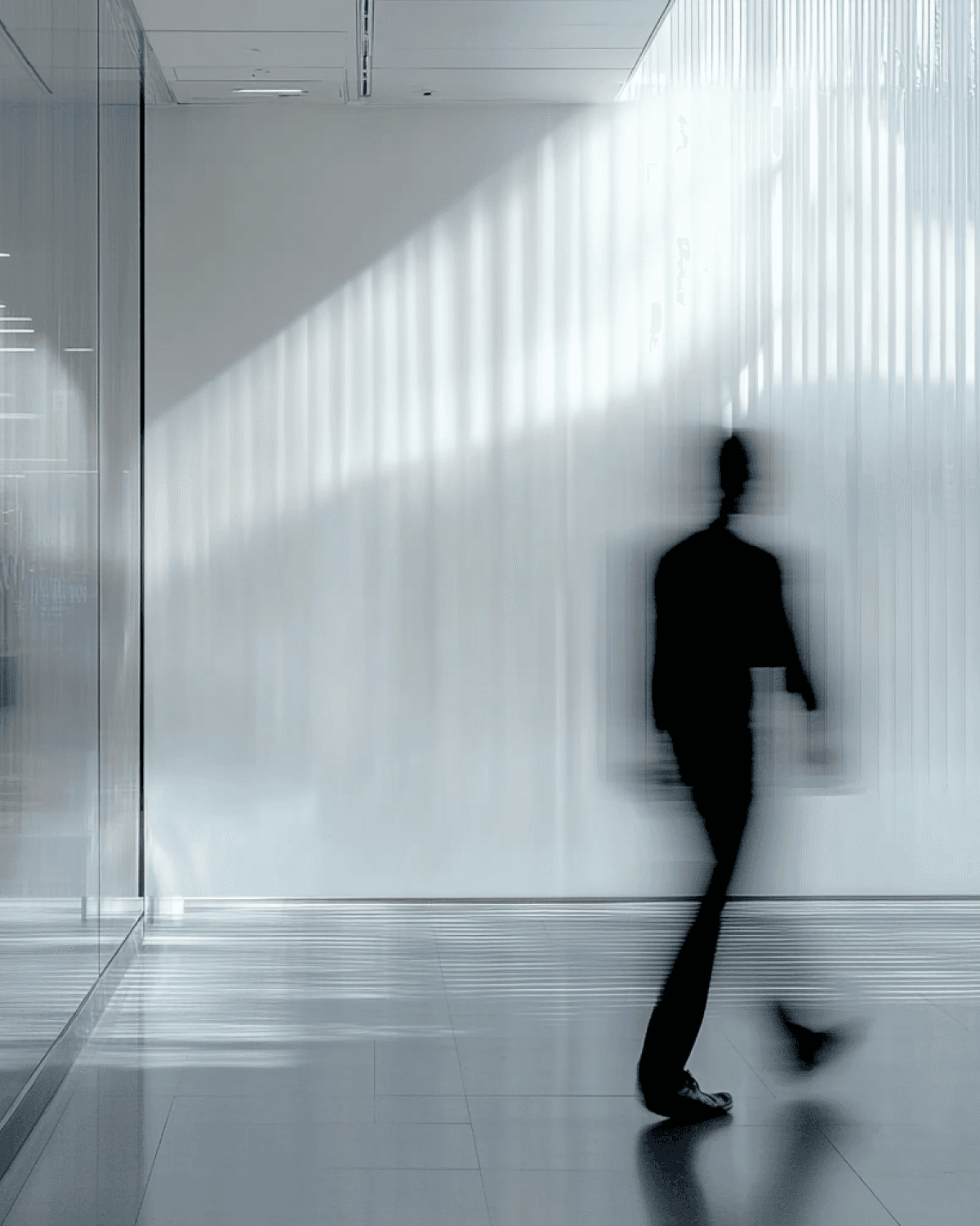 Abstract blurred silhouette of a person walking in a modern minimalist office hallway.