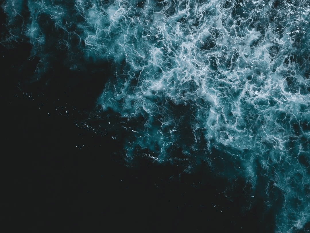 Aerial view of deep ocean waves crashing with white foam against dark blue water.