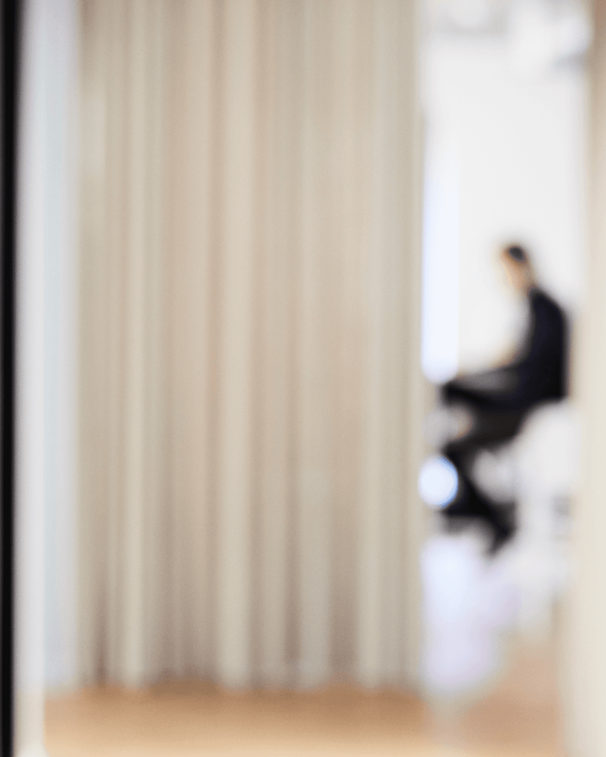 Abstract blurred office scene with a person sitting in the background behind light curtains.